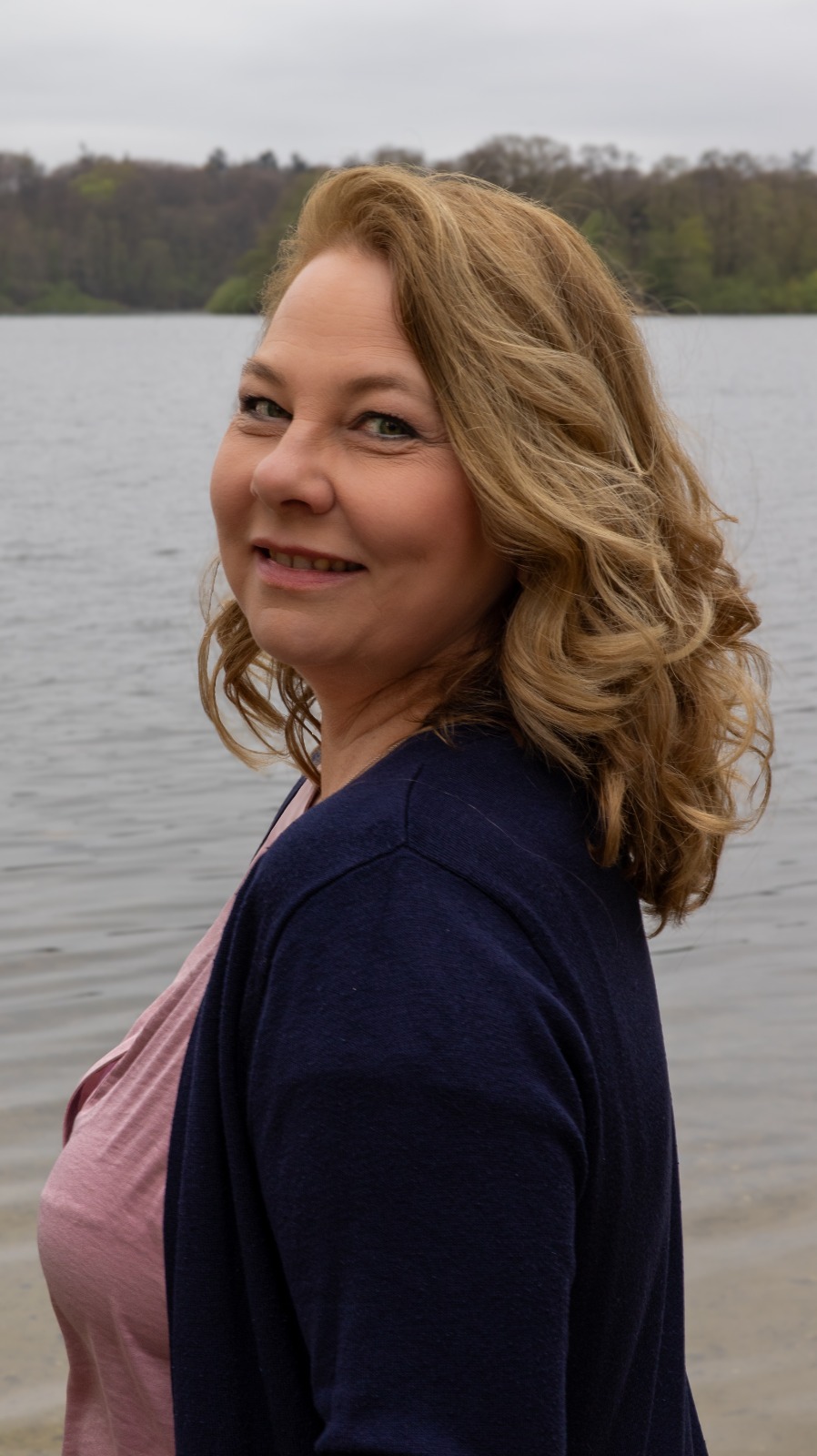 Stephanie Freyer lächelt offen am See, Blick über die Schulter